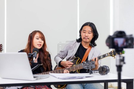 Téléchargez les photos : Musicien asiatique exécutant spectacle de rock en direct à la maison en utilisant la plate-forme en ligne pour fan et public au concert à domicile et en streaming réseau de diffusion - en image libre de droit