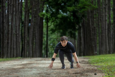 Asiatischer Trailrunner läuft im Freien auf einem Feldweg im Kiefernwald für Training und Workout-Aktivitäten, während er sich auf die Startposition für einen gesunden Lebensstil und Fitness konzentriert