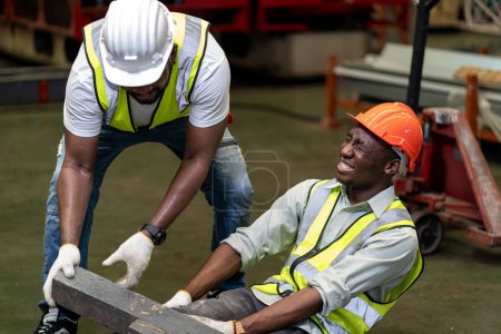 Téléchargez les photos : Ouvrier d'usine afro-américain ayant un accident tout en travaillant sur le site de fabrication tandis que son collègue aide à la sécurité sur le lieu de travail et d'urgence - en image libre de droit