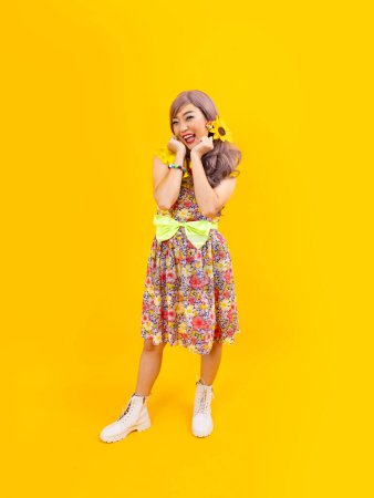 Foto de Vestido de mujer hippie asiático en la moda vintage de los años 80 con ropa retro colorida mientras posa aislado sobre un fondo amarillo para una fiesta de disfraces de lujo y cultura pop - Imagen libre de derechos