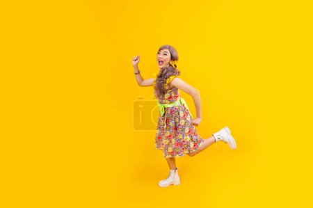 Téléchargez les photos : Asiatique hippie femme robe dans les années 80 mode vintage avec des vêtements rétro colorés tout en dansant et en courant isolé sur fond jaune pour la fête de tenue de fantaisie et la culture pop - en image libre de droit