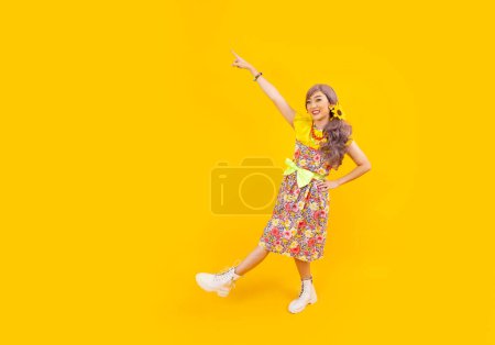 Téléchargez les photos : Asiatique hippie femme robe dans les années 80 mode vintage avec des vêtements rétro colorés tout en dansant isolé sur fond jaune pour la fête de tenue de fantaisie et la culture pop - en image libre de droit