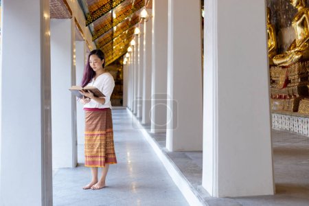 Asian buddhist woman is reading Sanskrit ancient Tripitaka book of Lord Buddha dhamma teaching while visiting the temple to chanting and worship inside monastery