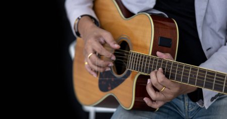 Téléchargez les photos : Gros plan du guitariste jouant de la guitare acoustique sur fond noir avec espace de copie pour la musique folklorique et une utilisation non branchée de la performance - en image libre de droit