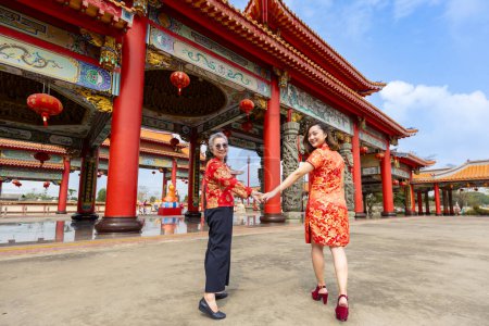 Vue arrière de la femme asiatique et sa mère aînée en robe rouge cheongsam qipao visite le temple bouddhiste chinois ensemble pendant le Nouvel An lunaire pour la culture traditionnelle