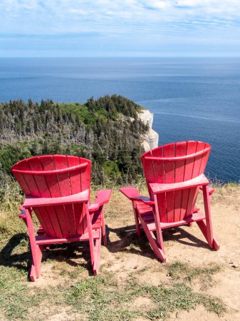 Foto de Mirando el Land 's End (Bout du monde) en el parque de Forillon, Gaspe, Quebec, Canadá. Dos sillas Adirondack rojas para que la gente admire el paisaje. - Imagen libre de derechos