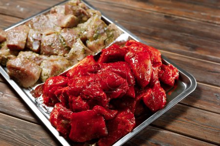 Auf dem Silberteller auf dem Holztisch liegt jede Menge rohes Fleisch. Der Koch bereitet Fleisch zum Braten zu.