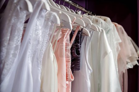 Hochzeitskleider und Kleider auf Kleiderbügeln im Geschäft auf violettem Hintergrund