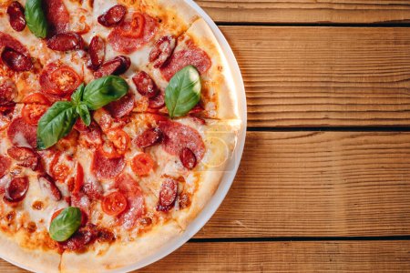 Foto de Podemos ver una pizza con queso frente a nosotros en la mesa. Hay un montón de salchichas, tomates, queso en la deliciosa pizza. Todo se ve increíble. La pizza se sirve al cliente.. - Imagen libre de derechos