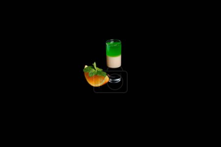 Photo for Layered strong cocktail in a glass. On black background. Decorated with orange and mint. - Royalty Free Image