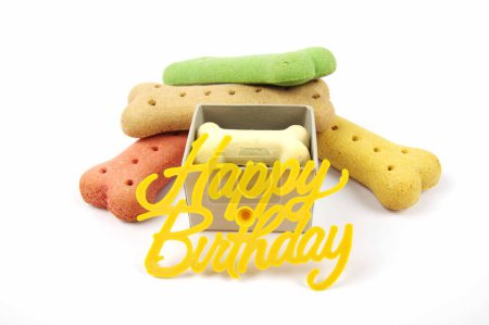 Téléchargez les photos : Biscuits pour chien d'anniversaire empilés derrière une boîte cadeau d'anniversaire avec un signe joyeux anniversaire sur un fond blanc - en image libre de droit