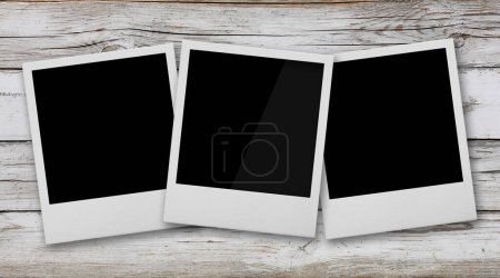 Nahaufnahme von drei leeren Polaroid-Instant-Fotorahmen auf weißem Grunge-Holztischhintergrund, erhöhte Ansicht von oben, direkt darüber