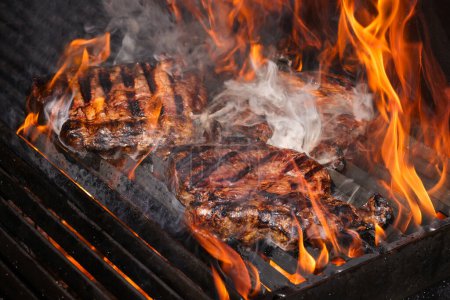 Photo for Close up searing and smoking ribeye beef steaks on open fire outdoor grill with cast iron metal grate, high angle view - Royalty Free Image