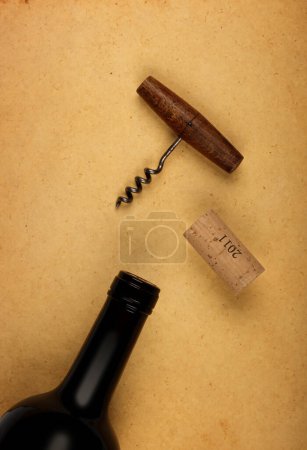 Photo for Close up one full unopen bottle of red wine with cork and retro opener with wooden handle over vintage brown paper background with copy space, high angle view - Royalty Free Image