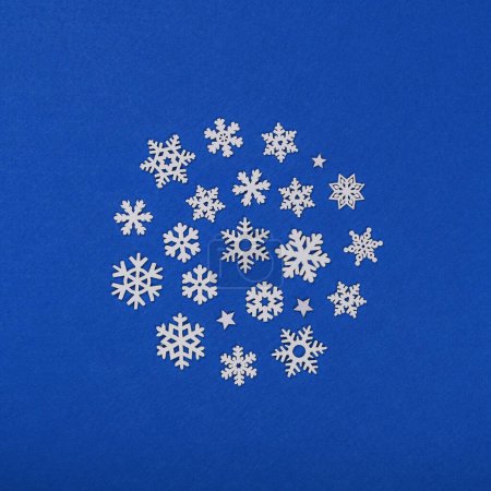 Photo for Close up circle of white wooden snowflakes Christmas decoration over blue felt background, table top view, flat lay - Royalty Free Image