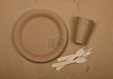Photo for Close up disposable paper plates, takeaway coffee cups and wooden forks on brown paper background, natural eating and drinking utensils, close up, elevated table top view, directly above - Royalty Free Image