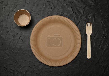 Photo for Close up empty disposable brown paper plate, takeaway coffee cup and wooden fork on black background, natural eating and drinking utensils, close up, elevated table top view, directly above - Royalty Free Image