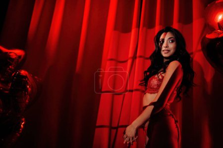 Foto de Rizado negro pelo asiático sensual modelo bajo luz y sombra de persianas en la piel posando en rojo glamour fondo. - Imagen libre de derechos