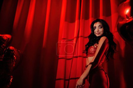 Foto de Rizado negro pelo asiático sensual modelo bajo luz y sombra de persianas en la piel posando en rojo glamour fondo. - Imagen libre de derechos