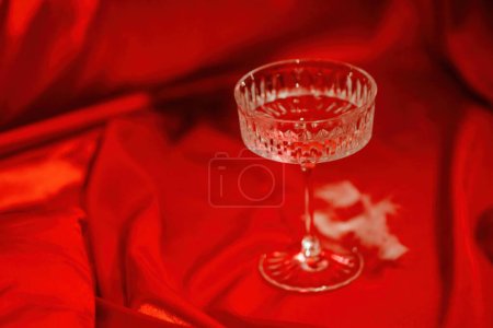 Extravaganter Glamour-Hintergrund mit Coupé-Glas Sekt für die Liebesparty bei gedämpftem Licht. Schöne romantische burleske Ort für Valentinstag Urlaub in roter Seide glänzenden Laken
