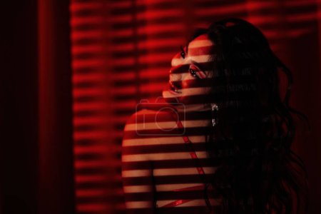 Foto de Rizado negro pelo asiático sensual modelo bajo luz y sombra de persianas en la piel en rojo glamour fondo. - Imagen libre de derechos