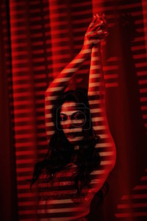 Foto de Sexy mujer asiática en ropa interior de encaje bajo la luz y la sombra de persianas en rojo glamour fondo - Imagen libre de derechos
