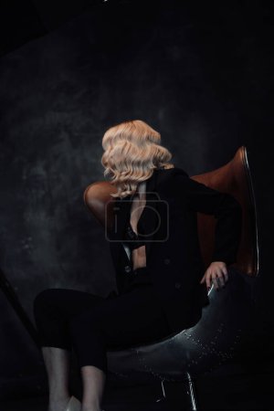 Photo for Young adult beauty woman in formal evening suit of black color with lace bra at thoughtful. Stylish blonde curly hair sensual model fashionista posing at studio in fashion pantsuit - Royalty Free Image