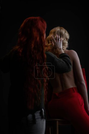 Photo for Adult beauty woman bare back in formal evening red trousers sitting pose without bra. Stylish blonde curly hair sensual nude model fashionista posing at studio in fashion pantsuit out of blazer - Royalty Free Image