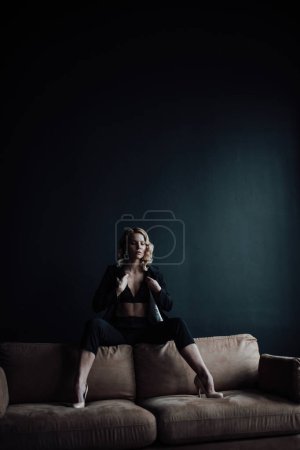 Téléchargez les photos : Young adult beauty woman in formal evening suit of black color with lace bra at thoughtful. Stylish blonde curly hair sensual model fashionista posing at studio in fashion pantsuit - en image libre de droit