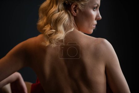 Foto de Adult beauty woman bare back in formal evening red trousers sitting pose without bra. Stylish blonde curly hair sensual nude model fashionista posing at studio in fashion pantsuit out of blazer - Imagen libre de derechos