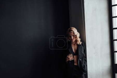 Photo for Adult beauty woman in formal evening suit of black color with lace bra taking photo for social media. Stylish blonde curly hair model fashionista posing in fashion pantsuit no shirt video calling - Royalty Free Image