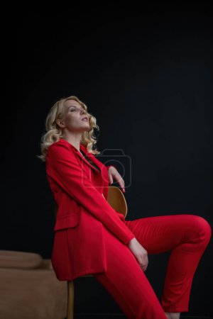 Foto de Mujer joven de belleza adulta en traje de noche formal de color rojo con ropa interior de encaje sujetador negro de pie por reflexivo. Elegante modelo de pelo rizado rubia fashionista posando en el estudio en traje pantalón de moda - Imagen libre de derechos