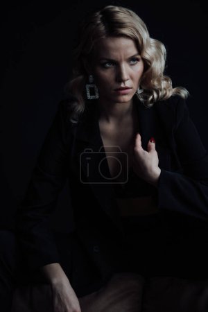 Photo for Young adult beauty woman in formal evening suit of black color with lace bra at thoughtful. Stylish blonde curly hair sensual model fashionista posing at studio in fashion pantsuit - Royalty Free Image