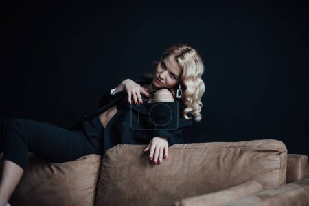 Foto de Young adult beauty woman in formal evening suit of black color with lace bra at thoughtful. Stylish blonde curly hair sensual model fashionista posing at studio in fashion pantsuit - Imagen libre de derechos