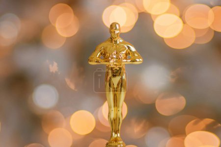 Hollywood gold oscars trophy figurine imitation seen during an award cinema ceremony. Success and victory concept close up statuette at twinkle yellow lights background