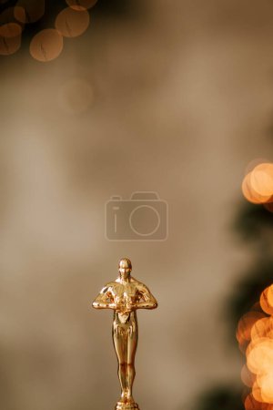 Téléchargez les photos : Hollywood gold oscars trophy figurine imitation seen during an award cinema ceremony. Success and victory concept close up statuette at twinkle yellow lights background - en image libre de droit