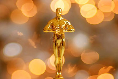 Téléchargez les photos : Hollywood gold oscars trophy figurine imitation seen during an award cinema ceremony. Success and victory concept close up statuette at twinkle yellow lights background - en image libre de droit