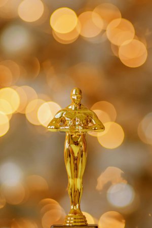 Photo for Hollywood gold oscars trophy figurine imitation seen during an award cinema ceremony. Success and victory concept close up statuette at twinkle yellow lights background - Royalty Free Image