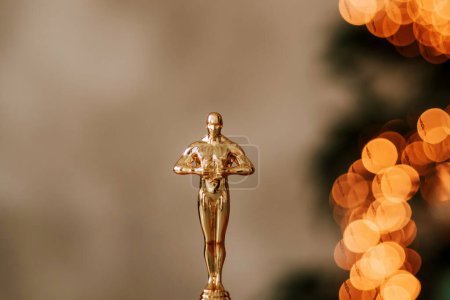 Photo for Hollywood gold oscars trophy figurine imitation seen during an award cinema ceremony. Success and victory concept close up statuette at twinkle yellow lights background - Royalty Free Image