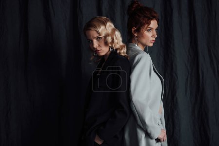 Photo for Adult beauty elegant multi ethnic young girls in formal evening suits of different colors with bra. Stylish blonde and redhead sensual fashionistas posing at studio in fashion pantsuits no shirts - Royalty Free Image