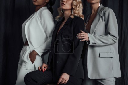 Photo for Adult beauty elegant multi ethnic group young girls in formal evening suits of different colors with bra. Stylish diverse people sensual fashionistas posing at studio in fashion pantsuits no shirts - Royalty Free Image