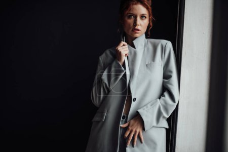 Photo for Adult beauty elegant young woman in formal evening gray suit with white bra at thoughtful. Stylish ginger curly hair sensual model bare shoulder fashionista posing at studio in fashion pantsuit - Royalty Free Image