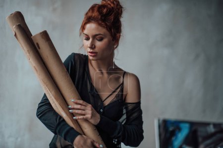Photo for Adult beauty elegant young woman in formal evening black blouse. Stylish ginger curly hair sensual model bare shoulder fashionista posing with paint palette and brushe hugs painting rolls at studio - Royalty Free Image