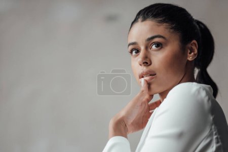 Photo for Young adult beauty swarthy woman in formal evening white suit no shirt hand on face touching. Stylish black curly hair sensual african american model fashionista posing at studio in fashion pantsuit - Royalty Free Image