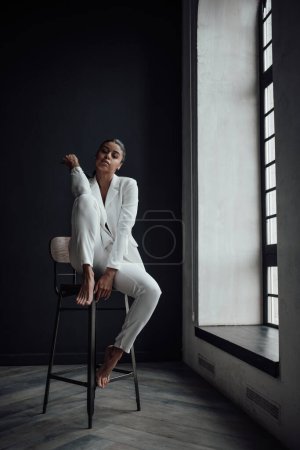 Young adult beauty swarthy woman in formal evening white suit with bra at thoughtful. Stylish black curly hair sensual african american model fashionista posing at studio in fashion pantsuit