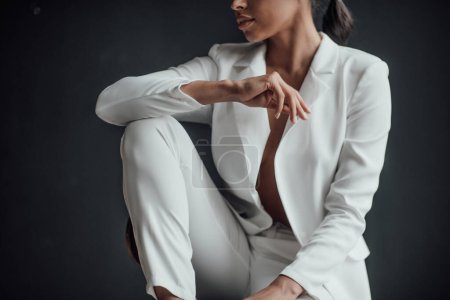 Young adult beauty swarthy woman in formal evening white suit no shirt hand on face touching. Stylish black curly hair sensual african american model fashionista posing at studio in fashion pantsuit