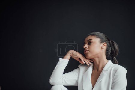 Photo for Young adult beauty swarthy woman in formal evening white suit no shirt hand on face touching. Stylish black curly hair sensual african american model fashionista posing at studio in fashion pantsuit - Royalty Free Image