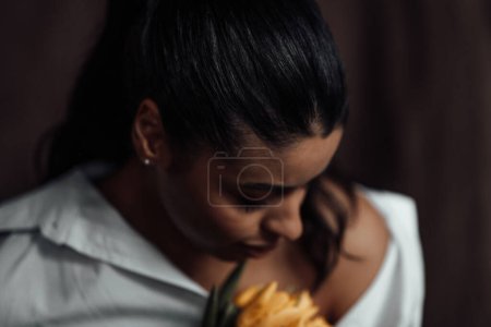 Photo for Young adult beauty swarthy woman in white shirt bare shoulder hugs bouquet of yellow tulips. Stylish black curly hair sensual african american model fashionista posing in studio at spring holidays - Royalty Free Image