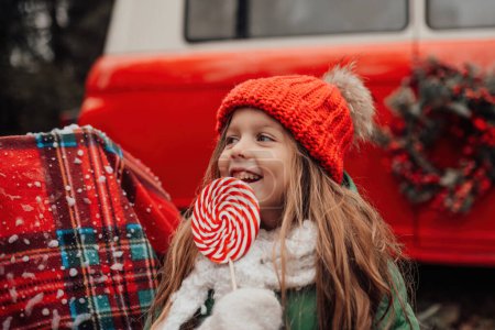 Photo for Female child celebrating Christmas and New Year winter holidays season outdoor. Active little girl in red knitted hat joyful spending time on open air with Xmas candy cane in hands - Royalty Free Image