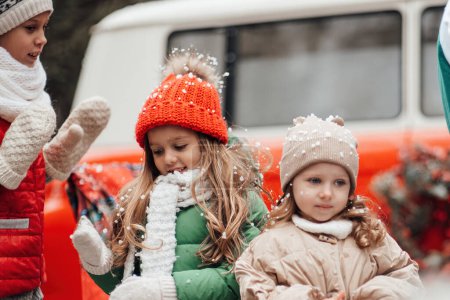 Photo for Female children celebrating Christmas and New Year winter holidays season outdoor. Active kids joyful spending time together having fun near Xmas bus rejoices at first snow enjoying childhood - Royalty Free Image